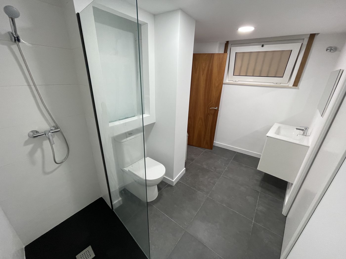 Bathroom with white walls, dark large-format floor tile and walk-in shower with black tray
