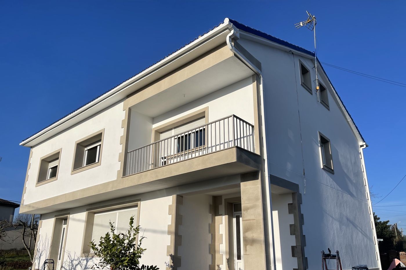 Two-story house after exterior renovation with white render, stone-look trims and new gutters