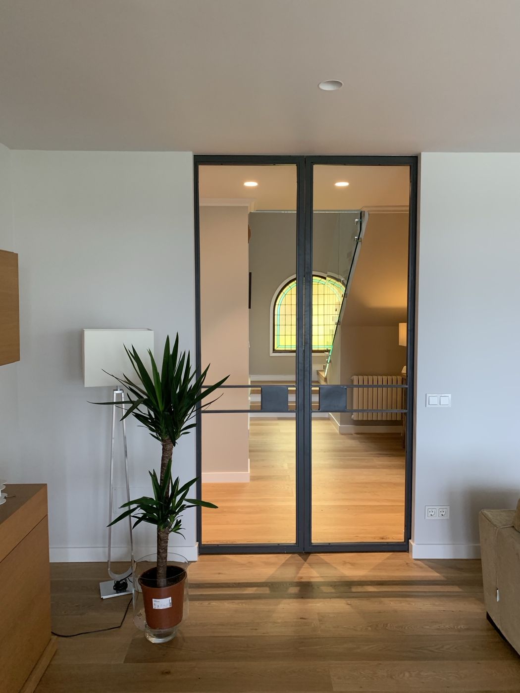Steel-framed glass doors opening onto an oak-floored hall and glass-railed staircase