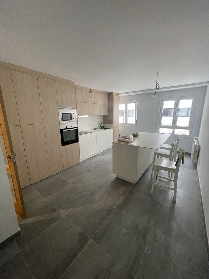 Kitchen with oak tall cabinets, white handleless base units and island with seating on large-format tile