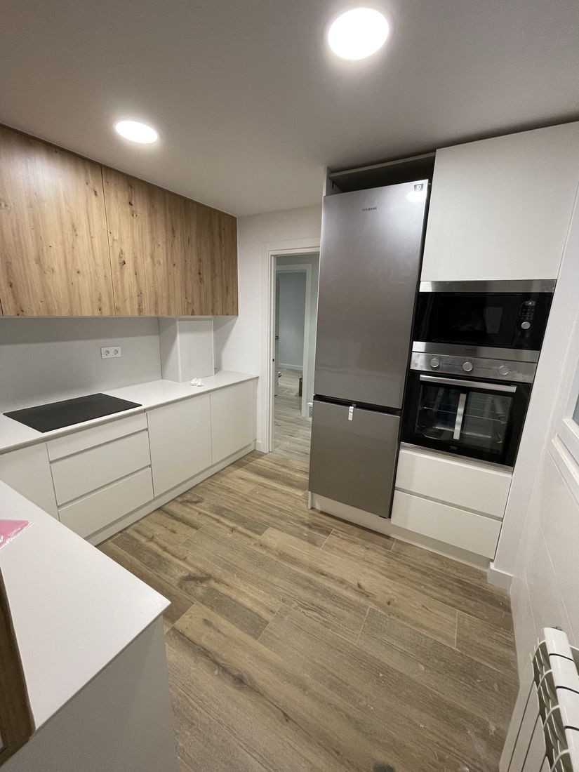 U-shaped kitchen with oak upper cabinets, white handleless base units and built-in oven