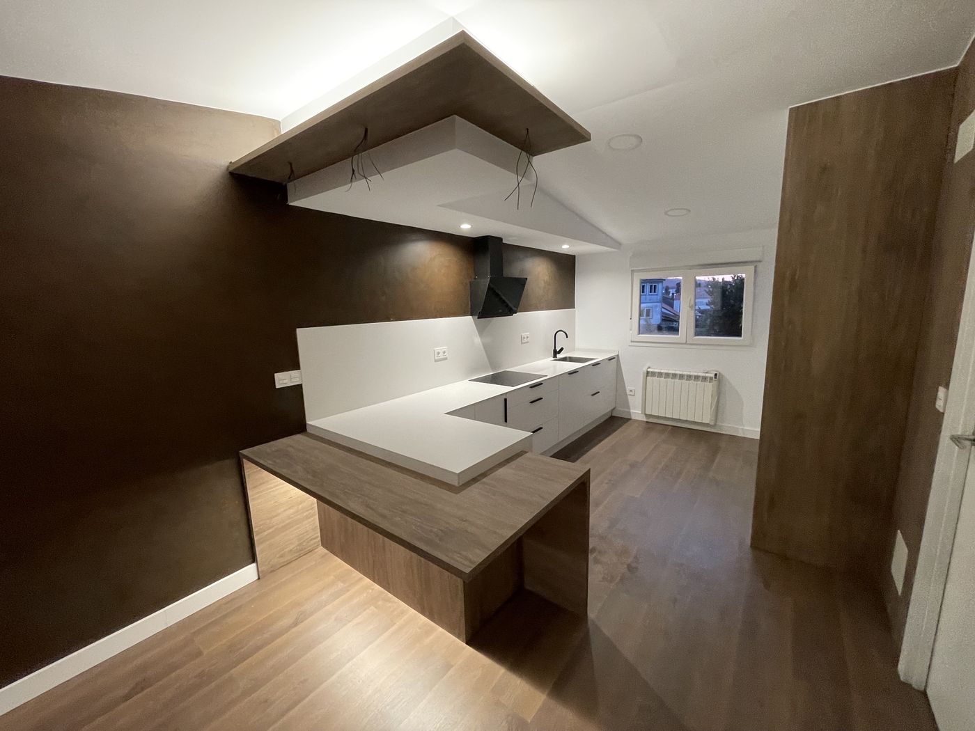 Kitchen with white countertops, wood-look peninsula, bronze feature wall and dropped ceiling with LED