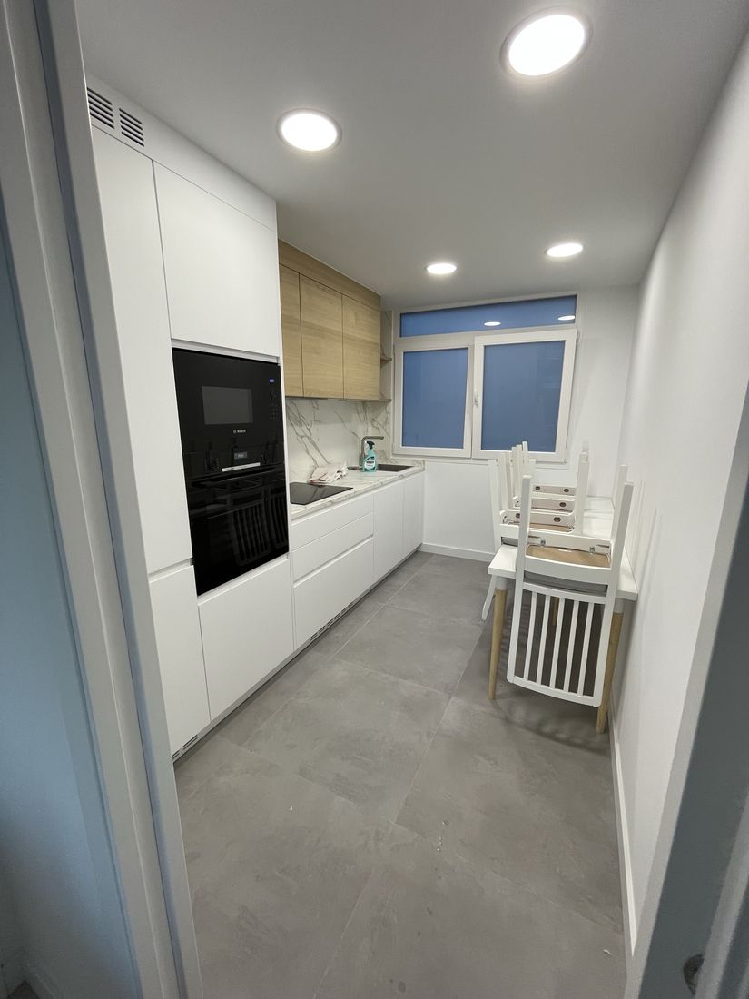 Galley kitchen with handleless white cabinets, oak wall units and marble-look backsplash