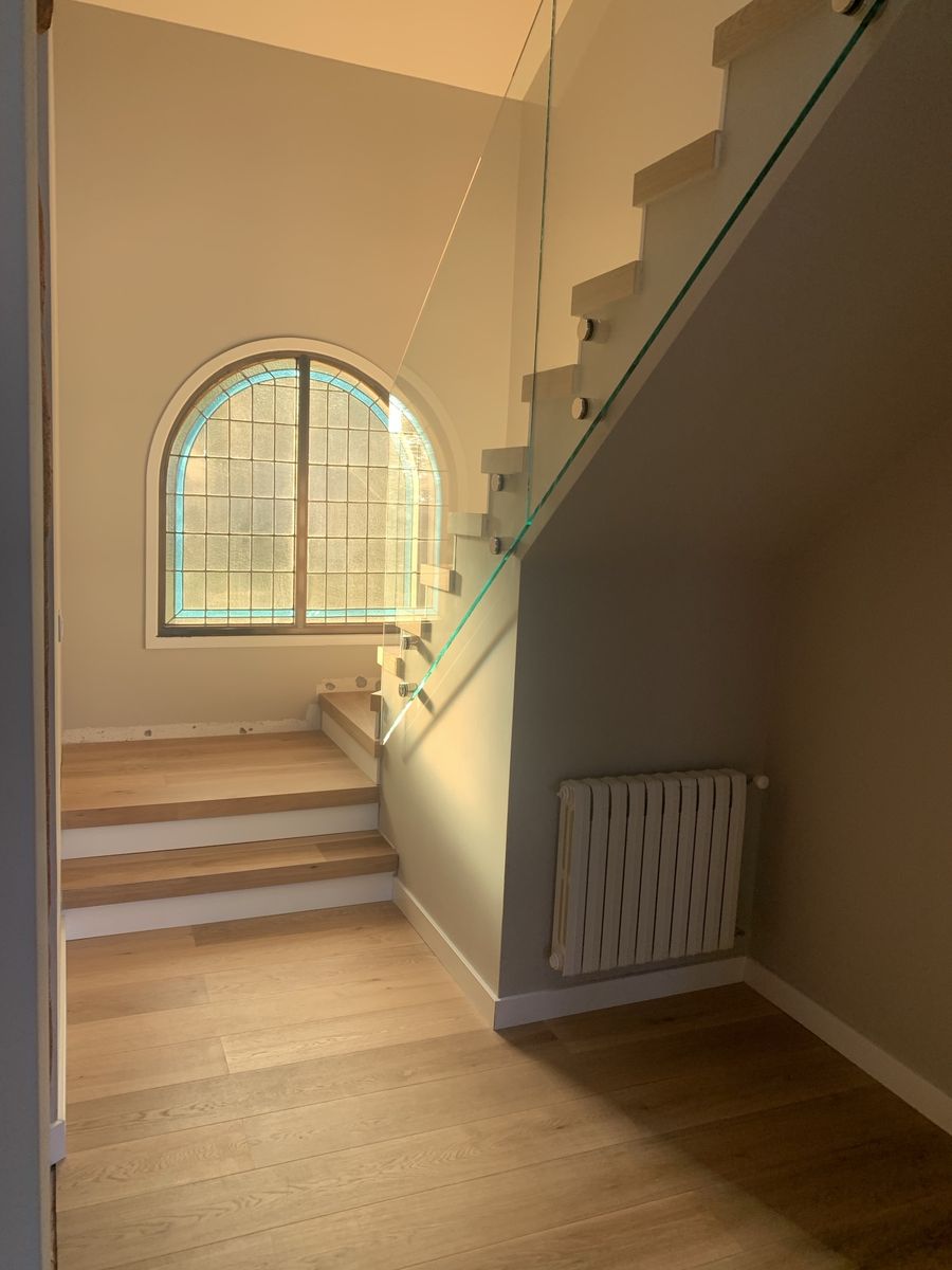Staircase with oak treads, frameless glass railing and restored stained-glass arched window